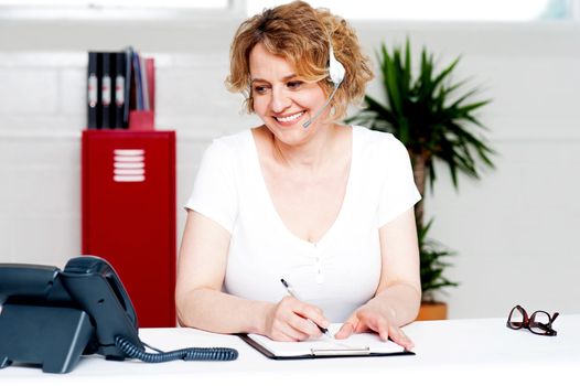 Cheerful customer support executive at work writing down customer complaints