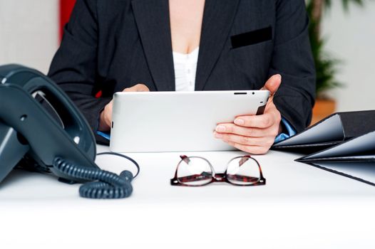 Cropped image of woman holding tablet device seated in office at work desk