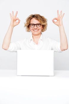 Corporate lady showing excellent gesture to camera sitting in front of laptop