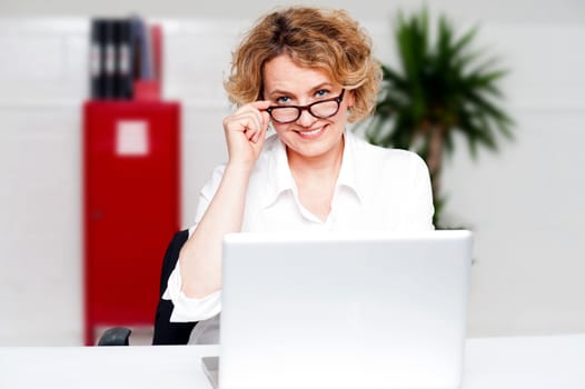 Happy aged woman holding glasses working on laptop, business concept