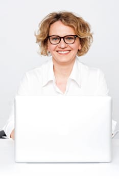 Smiling businesswoman sitting in front of laptop looking at camera