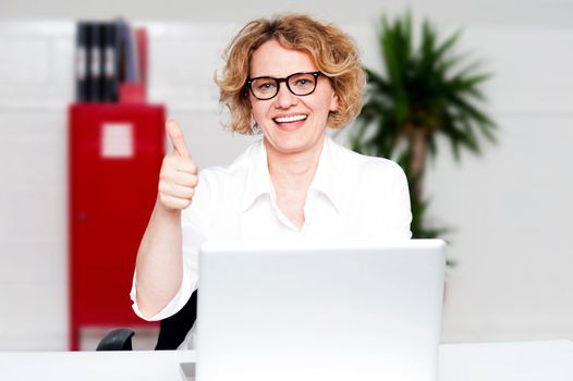 Successful businesswoman seated in office gesturing thumbs up to camera