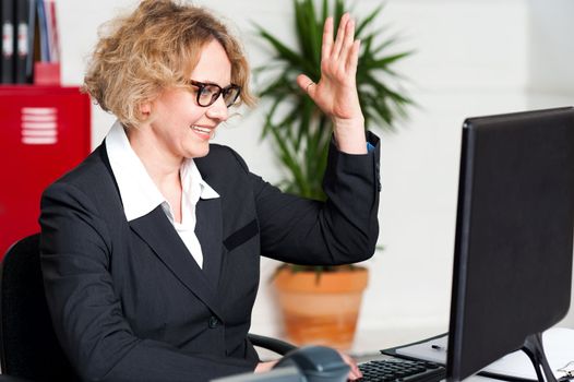 Smiling woman with raised arm looking at screen and typing on keyboard with other hand
