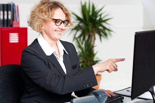 Cheerful woman pointing at something on computer screen