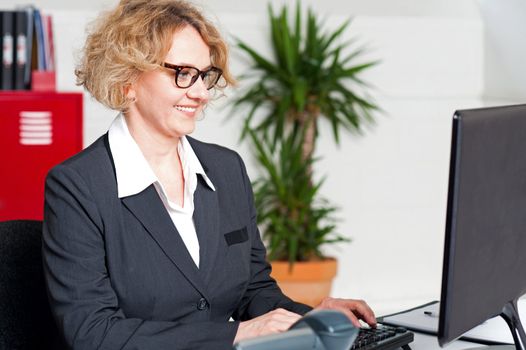 Aged woman in office wearing eyeglasses working on computer