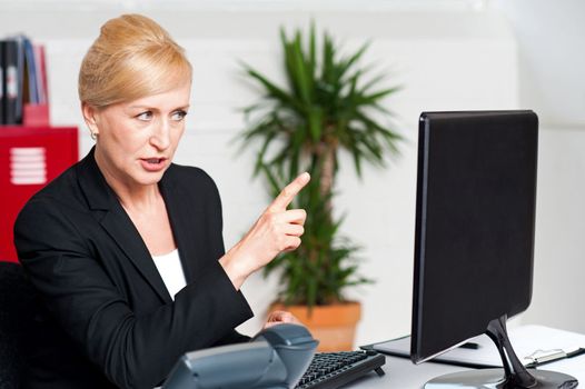 Angry woman in office indicating at computer led screen