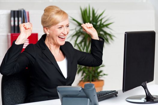 Excited corporate lady with raised arms looking at computer screen