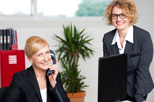 Seated woman attending call with colleague beside her, cheerful business team