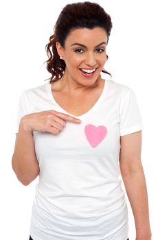 Cheerful girl pointing at pink paper heart on her t-shirt. Love concept