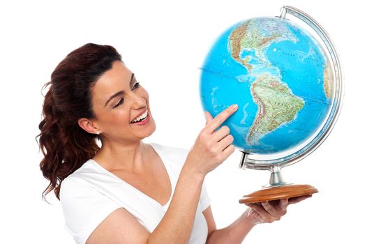 Smiling woman holding globe in one hand and pointing at Pacific Ocean