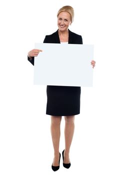 Female executive pointing towards blank white ad board and smiling at camera