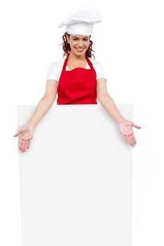 Female chef posing behind blank white billboard with her hands leaning in front of ad board