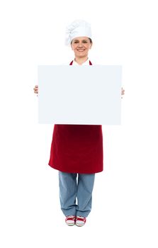 Smiling chef displaying white advertising board, full length portrait