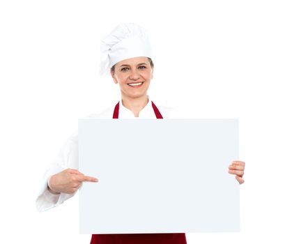 Isolated smiling female chef pointing towards blank whiteboard