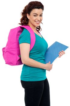 Side view of attractive smiling college girl carrying backpack and holding spiral notebook