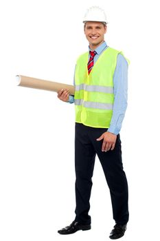 Smiling young architect holding blueprints, wearing helmet and safety jacket