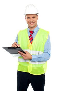 Smiling young construction engineer with safety hat writing on notepad against white background
