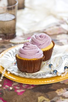 Violet cupcake with violet cream on top by coffee