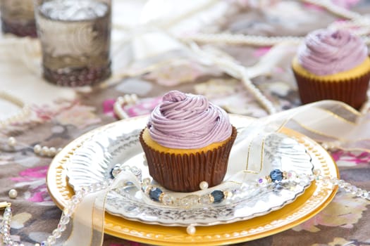 Violet cupcake with violet cream on top by coffee