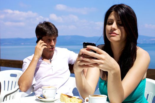 Woman texting man talking on cellphone during breakfast on a lake