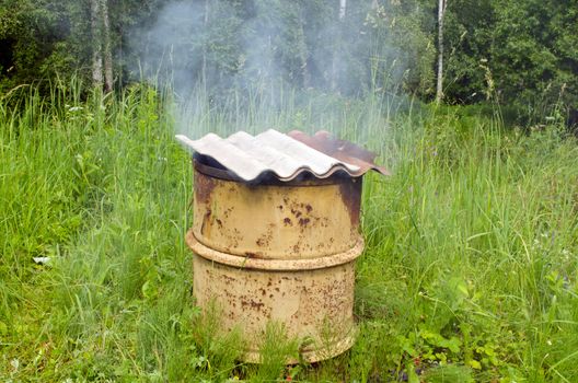 Smoke rises from old rural handmade barrel smokehouse asbestine slate roof.