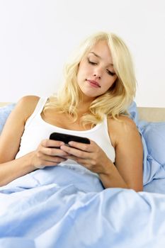 Blonde woman reading text message on phone in bed at home