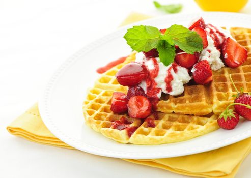 Plate of belgian waffles with fresh strawberries and whipped cream