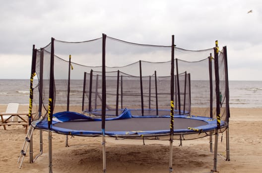 Trampolines with protective net wall on beach coast sand. Active recreation near sea.