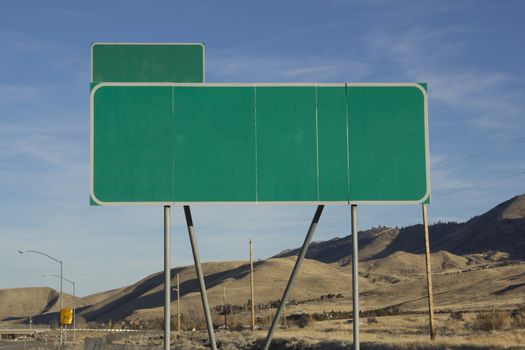 Green road sign with a blue sky and mountain background.