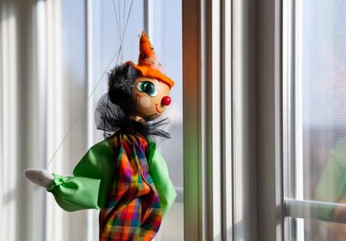 Puppet or marionette hanging in window and gazing outside into sunlit exterior