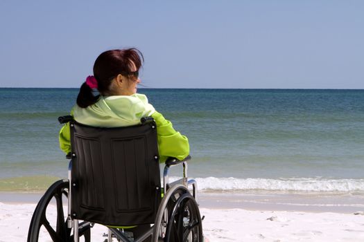Handicapped woman sits disabled in her wheelchair at the beach.