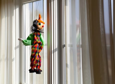 Puppet or marionette hanging in window and gazing outside into sunlit exterior
