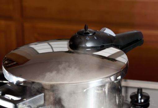 Pressure cooker releasing steam pressure on hob in modern kitchen
