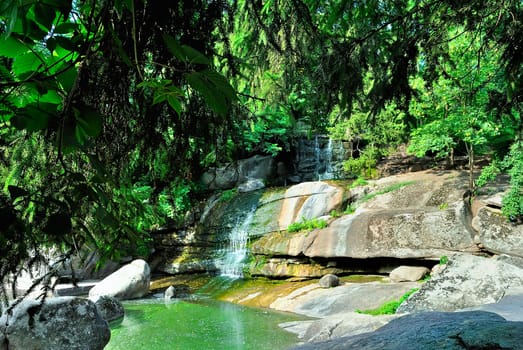 Small waterfall on a summer day among the rocks and green trees