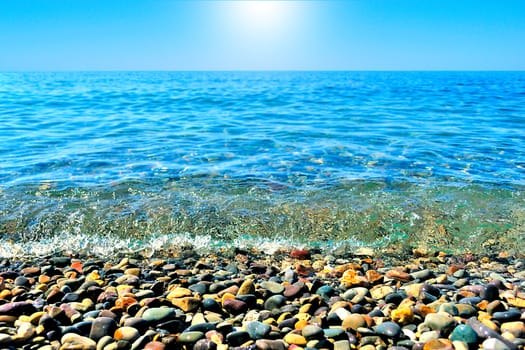 Marine blue wave in the bright sun on the pebbly beach