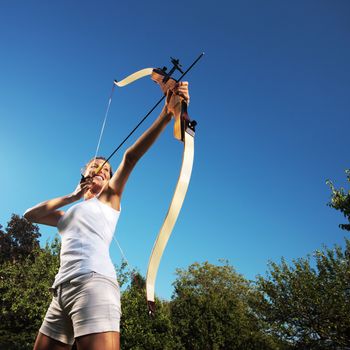 Attractive woman bending a bow and aiming in the sky