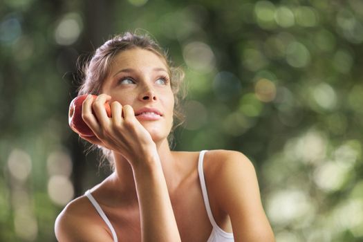 Portrait of young beautiful woman holding an red apple on green background summer nature.