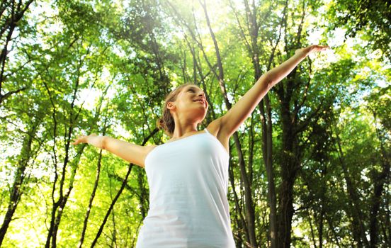 Young beautiful woman arms raised enjoying the nature in green forest