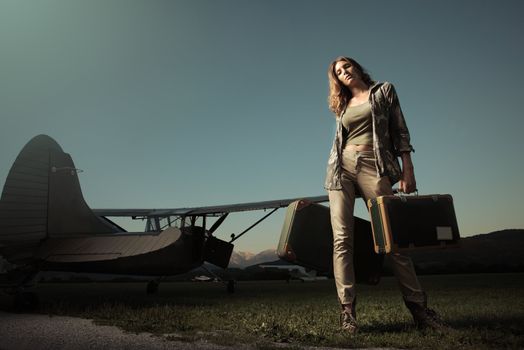 Fashion young woman with a suitcase. Airplane in the background.