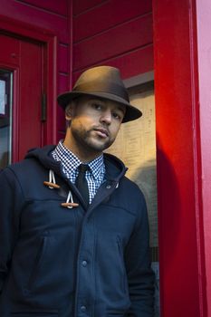 Young black man with fedora standing in red doorway looking at the camera.