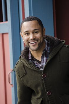 Portrait of young black man with smile, standing in red and blue doorway.