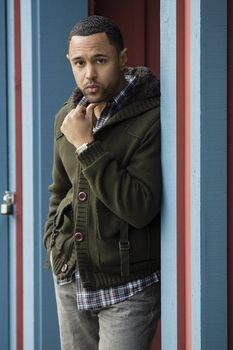 Young black man with hand on chin, standing in blue doorway with red trim.