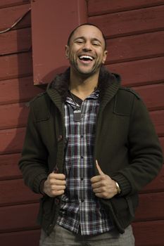 Young Black Man with big smile standing against red painted wall.