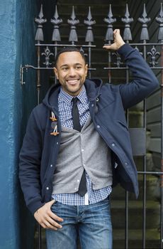 Young Black man standing against wrought iron fence with raised arm holding fence.