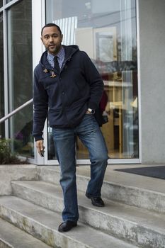 Young black man standing on light colored, store front steps looking into the camera.