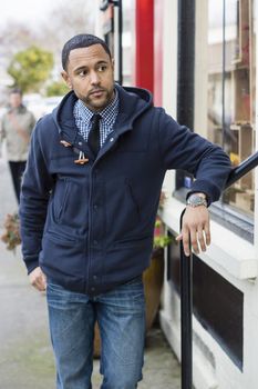 Black man standing in the street leaning of a railing and looking to the right.