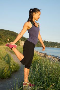 Young Women at the beach stretching on trail post with shoreline in background.