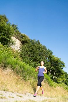 Young women running on beach trail with tall grass and trees in background.