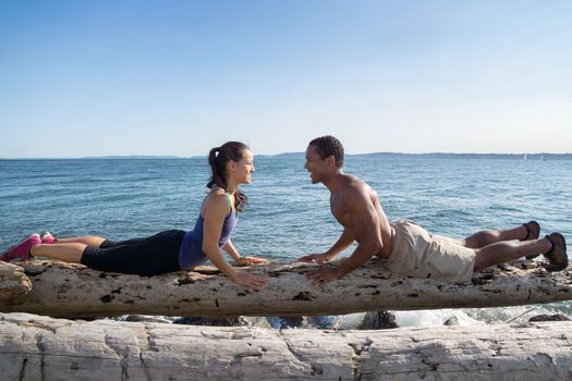 Young couple on beach, facing each other in Cobra yoga pose with water in background