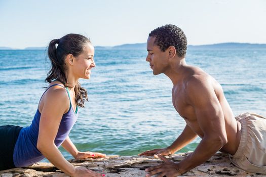 Close up of young couple on beach, facing each other in Cobra yoga pose with water in background